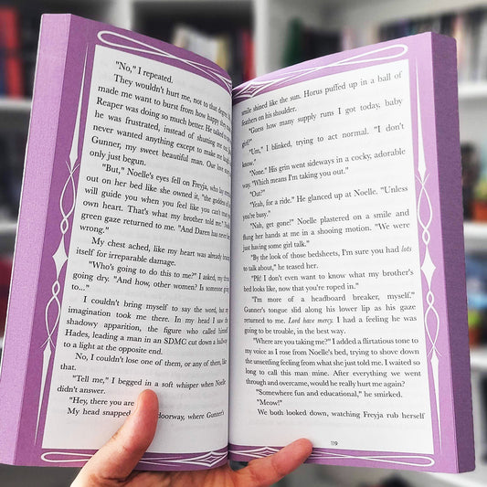 Open book with purple decorative edges held by a hand, with blurred background