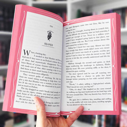 Open book with pink cover held by a hand, blurred background