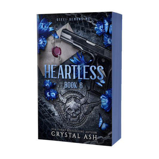 Book cover of 'Heartless' by Crystal Ash with a gun, skull, and blue flowers on a dark background.