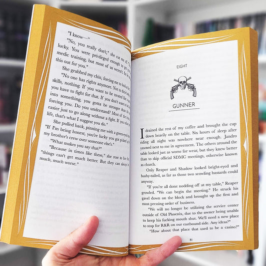 Open book with text and a gun illustration held by a hand.