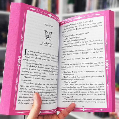 Open book with pink cover held by a hand, blurred background